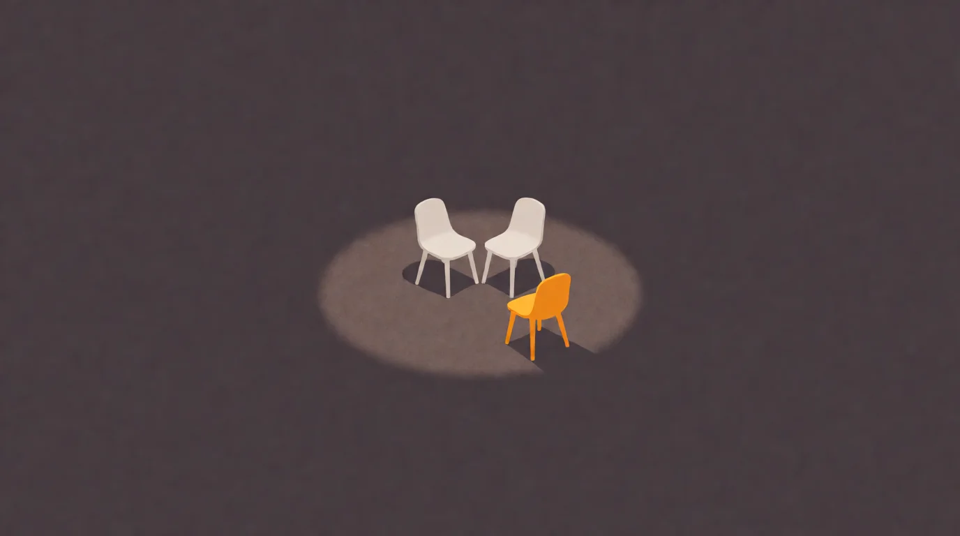 Two small off-white chairs facing each other in a warm pool of light, a third amber chair pulled up at the edge of the light facing them both